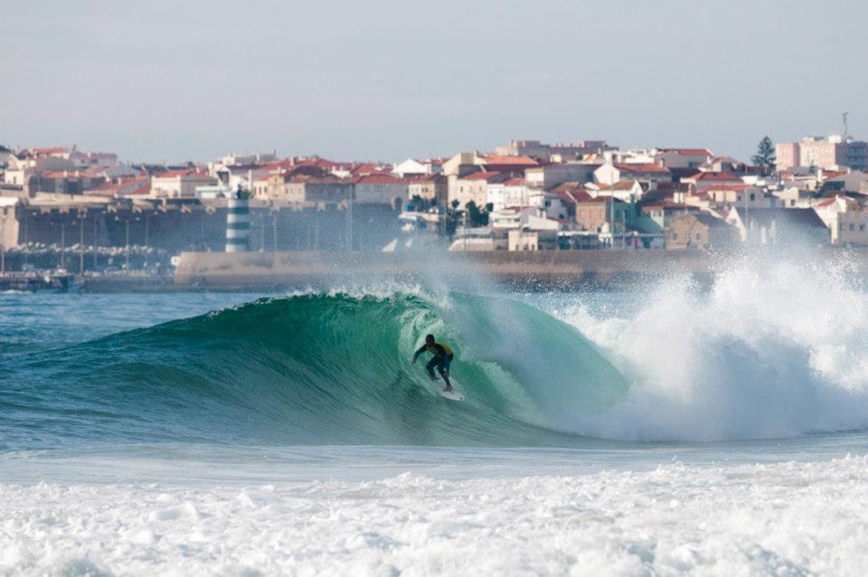 Surfer riding a barrel at Supertubos with Peniche behind